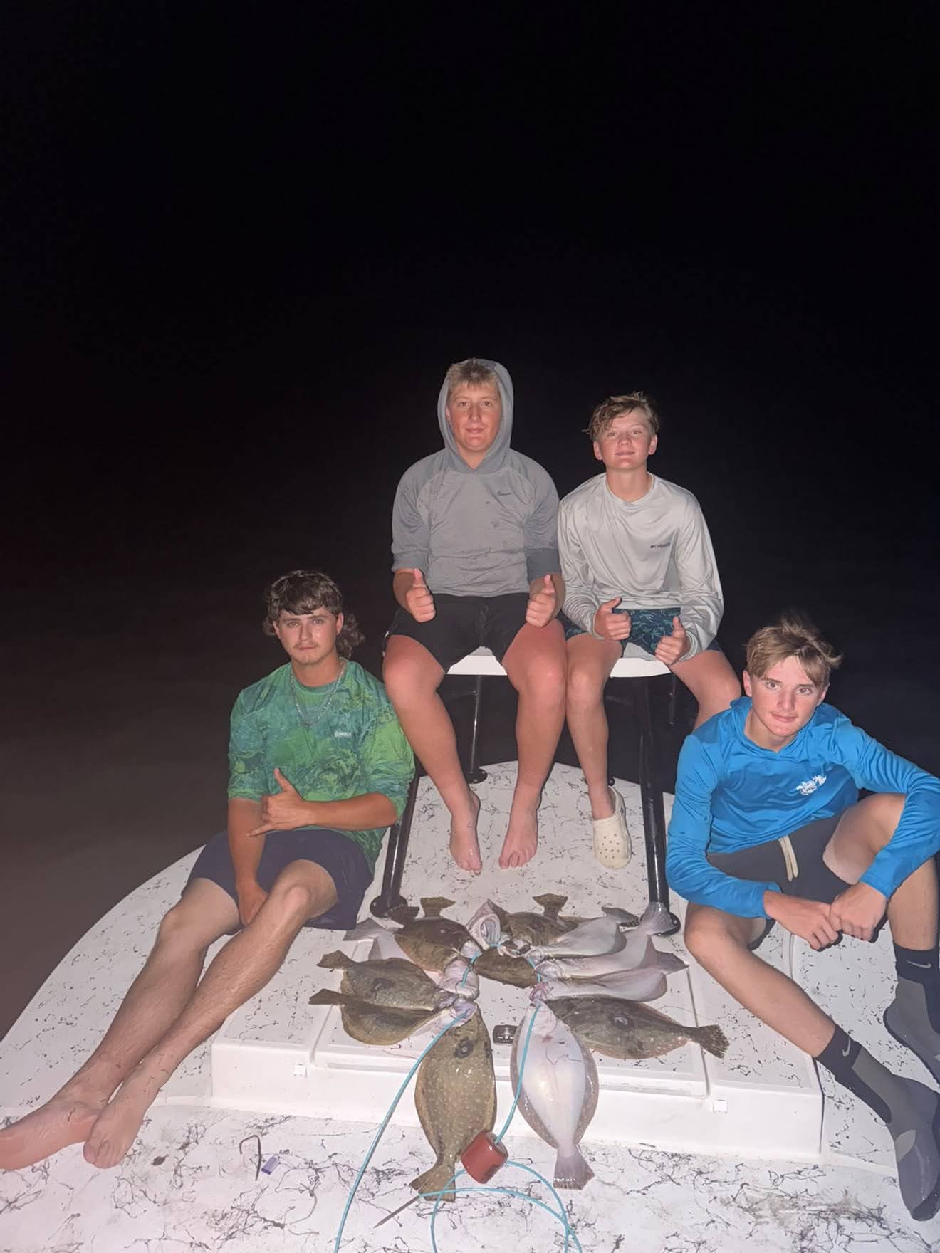 Four young anglers with flounder catch on boat at night